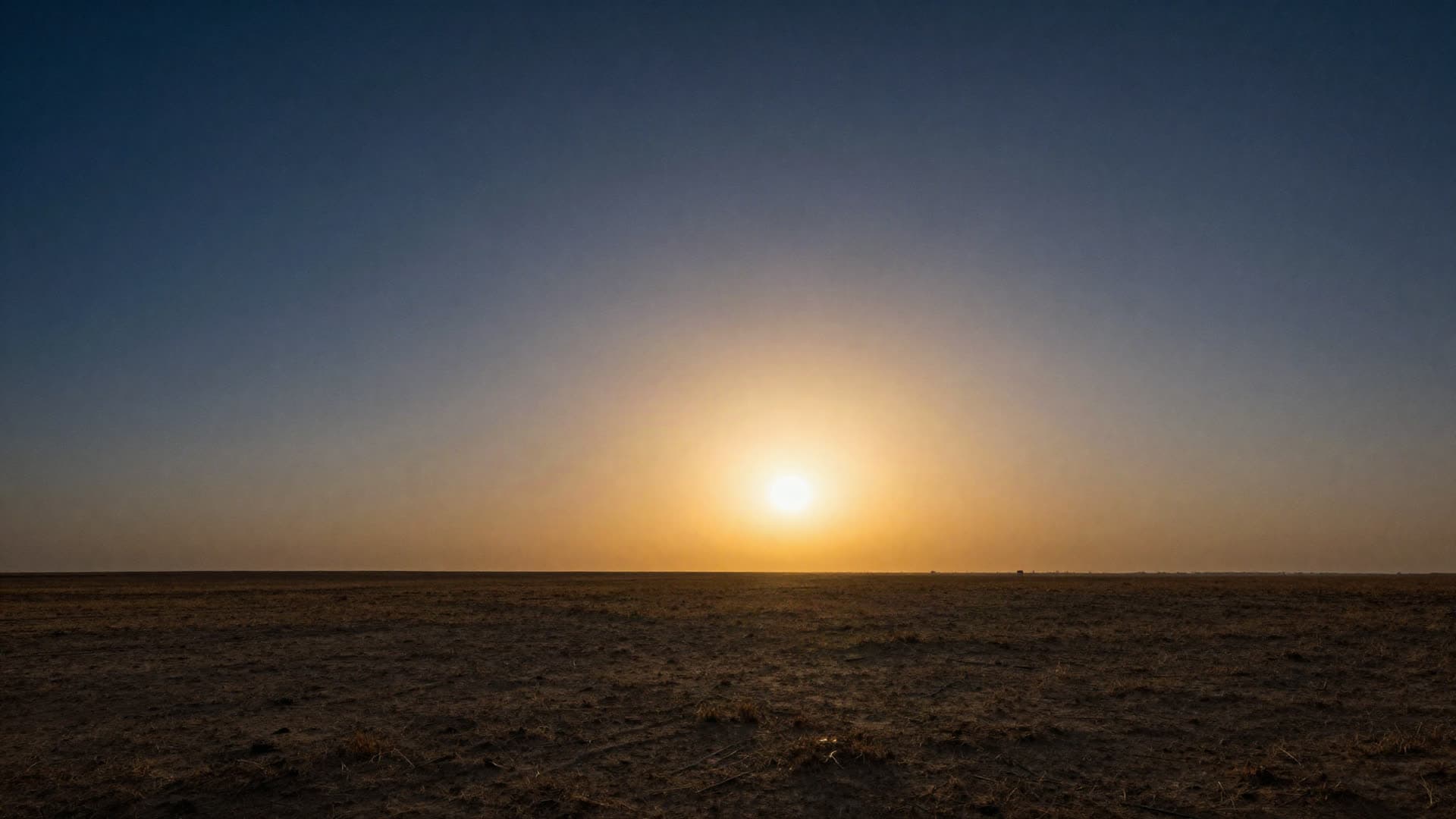 An immense empty plain at dawn under a single low light on the horizon, with nothing built on it.
