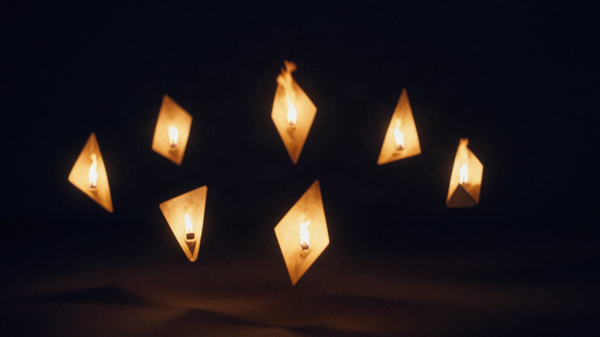 Seven points of flame suspended in a dark field, six of them angled toward the one in the centre.