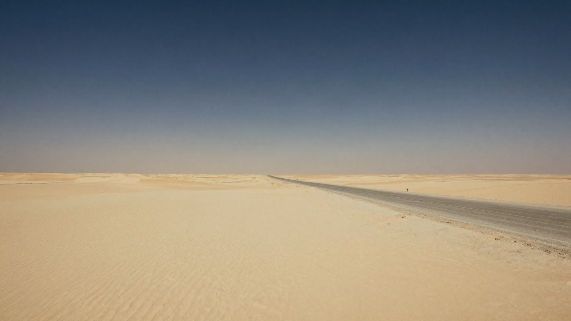 An open desert at midday with a single road running through it and heat haze on the horizon.